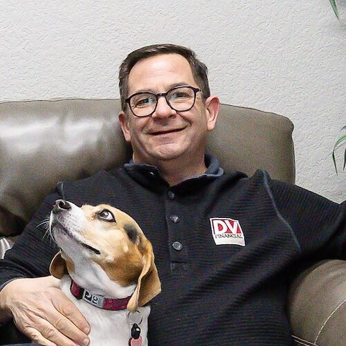 Art, a financial planner at DV financial, sitting on the couch smiling with Paisley the dog in his lap